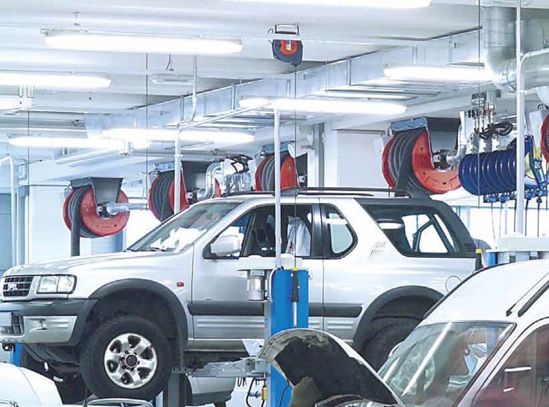 An auto workshop including cars and hanging hose reels for the vehicle exhaust extraction system